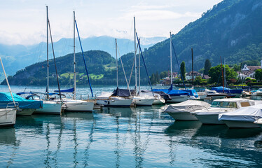 Fototapeta na wymiar Early morning in harbor. Сoastal town Gersau of Lake Lucerne and Swiss Alps. A lot of white boats and luxury yachts moored in marina on a turquoise water, during a summer season. Travel and vacation.