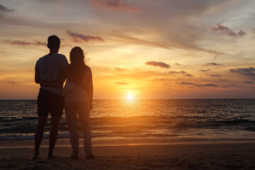 silhouette of young couple hugs on beach at orange sunset backside view copyspace