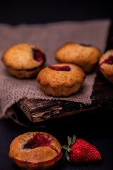 Cupcakes with white cream and strawberry on vintage blanket over black wooden background with fresh strawberries.