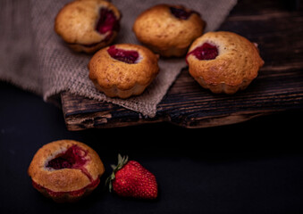 Cupcakes with white cream and strawberry on vintage blanket over black wooden background with fresh strawberries.