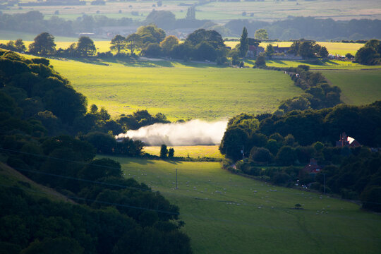 Agricultural fields and a fire burning, photographed from the Dyke, South Downs, Sussex, UK.