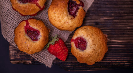 Tasty cupcake, decorated with fresh strawberry on a dark wooden background. Muffin with place for text.