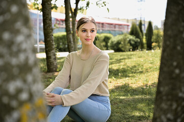 A model sits between trees in a summer park in sunny weather. Portrait of a caucasian girl with beauty makeup