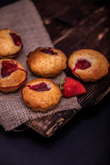 Tasty cupcake, decorated with fresh strawberry on a dark wooden background. Muffin with place for text.
