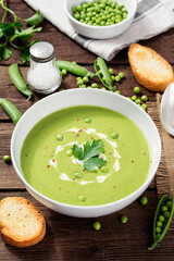 Bowl of  green peas cream soup on wooden table
