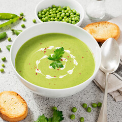 Bowl of green peas cream soup on gray stone background