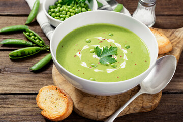 Bowl of  green peas cream soup on wooden table