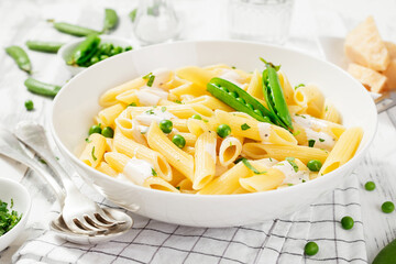 Pasta penne with fresh green peas and creamy sauce on white wooden background.