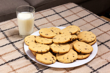 Delicious chocolate chip cookies plate with a glass of milk.  Sitting on a table with a blanket