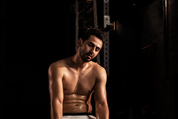 Fototapeta na wymiar Selective focus of good looking Caucasian sport man that gets sweat and exhausted after hard and long workout in a gym with dark tone background. Tired young muscle athlete with sweat in shadow tone