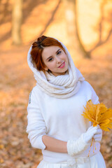 Portrait of a beautiful young redhead girl with flowers look attractive in a white dress on a background of autumn forest and leaves posing and smiling.
