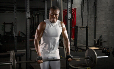 Fototapeta na wymiar Selective focus of young African athlete is doing exercise to build his biceps in a dark gym alone. African American man workouts by himself with dumbbell in shadow tone background