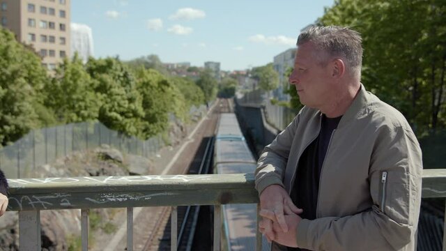 A middle-aged man talking on a bridge over the subway.