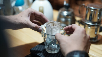 hand of barista preparing instant coffee drip on empty cup inside coffee shop bar