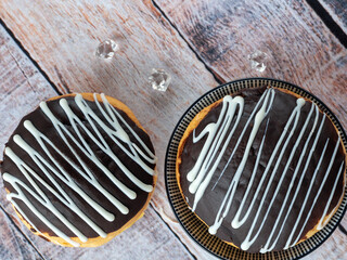 Two cakes on a color wooden table. The biscuits are decorated with chocolate and white icing. Background with cakes.