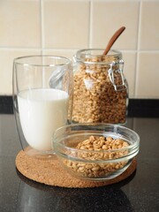 Breakfast from a bowl of wheat cereal, a glass of milk and a can of wheat cereal in the background on a cork stand