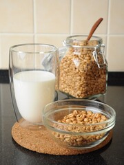 Breakfast from a bowl of wheat cereal, a glass of milk and a can of wheat cereal in the background on a cork stand