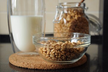 Breakfast from a bowl of wheat cereal, a glass of milk and a can of wheat cereal in the background on a cork stand