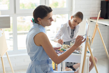 Fototapeta premium Concentrated girl draws on easel next to a young girl