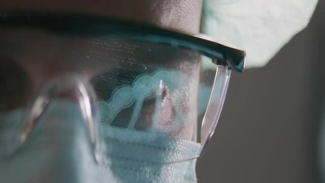 Male Scientist Works on Researching and Deciphering DNA Sequence on His Computer Display. We see a reflection in his protective laser glasses. Shot on RED EPIC-W 8K Helium.