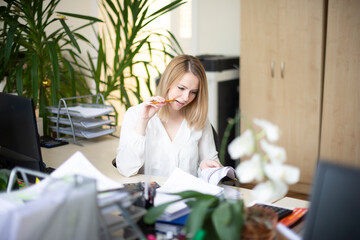 A young girl sits at a table in the modern office, holds a pencil in her hand and works with...