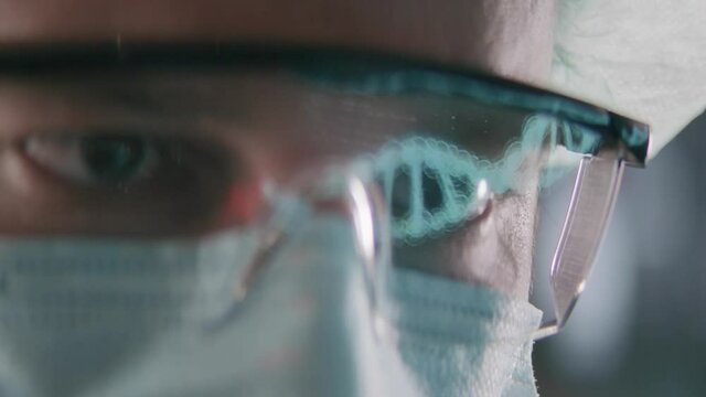 Male Scientist Works on Researching and Deciphering DNA Sequence on His Computer Display. We see a reflection in his protective laser glasses. Shot on RED EPIC-W 8K Helium.