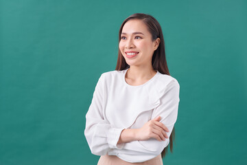 portrait of pretty asian girl smiling with arm crossed on turquoise background