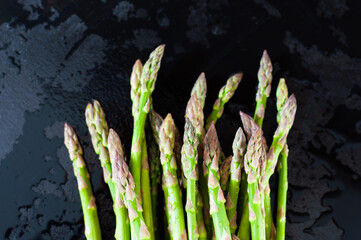 A small bunch of green asparagus sprouts in the center of the composition on a black wet background
