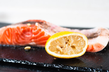 Salmon fillet seasoned with pepper and salt lies next to squeezed lemon on a stone stand
