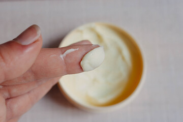 Skin and body care. Cream for the body, hands and feet, applied to the finger of a woman's hand on a natural white wooden background close-up with soft focus and a jar of cream in the background.