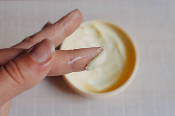 Skin and body care. Cream for the body, hands and feet, applied to the finger of a woman's hand on a natural white wooden background close-up with soft focus and a jar of cream in the background.