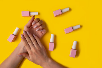 Gel polish of pink color and hands with manicure on a yellow background, top view