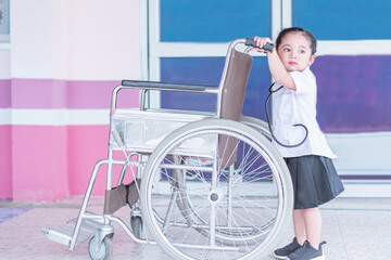 A Cute and lovely Asian baby girl in nurse uniform dress holding wheelchair