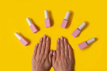 Gel polish of pink color and hands with manicure on a yellow background, top view