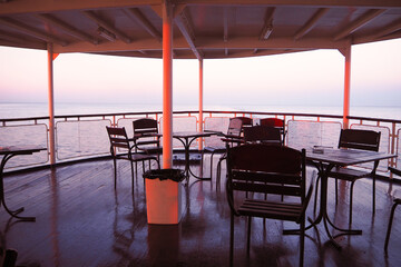 Deck of a old cruise ship on the high seas at sunset, empty tables and chairs, calm and pacification,  pink light of sun