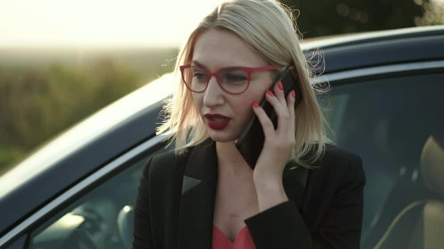 The blonde talking on the phone emotionally at car on highway at sunset