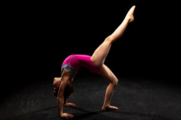Young gymnast posing on a black background. 