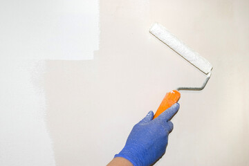 Repairs. A gloved hand holds a paint roller for painting the wall. Light streak. Real photo. Paint stained hand.