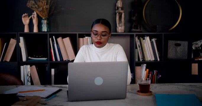Self isolation. Zoom in portrait of beautiful young African woman using laptop to work online from home slow motion.