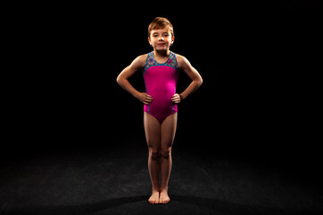 Young gymnast posing on a black background. 