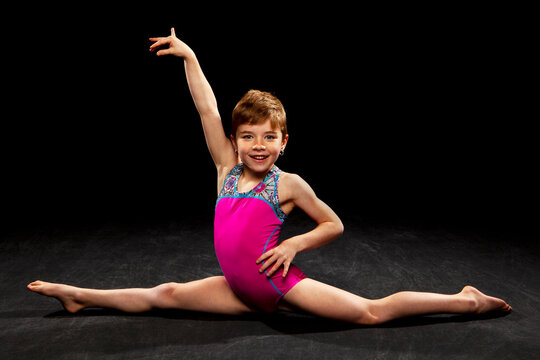 Young gymnast posing on a black background. 