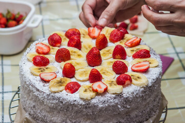 Hand crumbles cake with fruit. Homemade fruit cake with cream. Cake decorated with strawberries and bananas. Sprinkled with coconut on the sides.