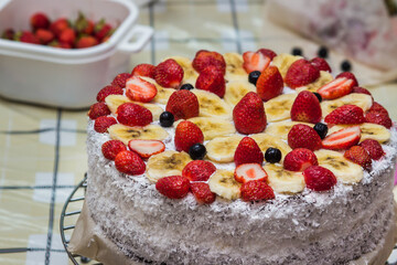 Homemade fruit cake with cream. Cake decorated with strawberries and bananas. Coconut sprinkled on the sides