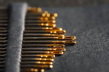 Gold sewing needles on a black background in a row.