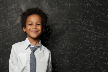 Smart kid student boy on chalkboard background with science formulas