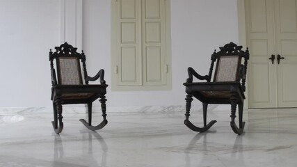two wooden chairs rocking in front of the colonial house. empty chair in the yard. vintage video concepts for historical, horror, spooky, legendary films and more - Powered by Adobe