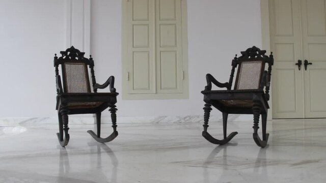 two wooden chairs rocking in front of the colonial house. empty chair in the yard. vintage video concepts for historical, horror, spooky, legendary films and more