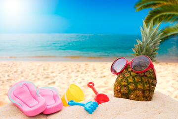 natural tropical pineapple wearing sunglasses with sandals and beach toys on the sand