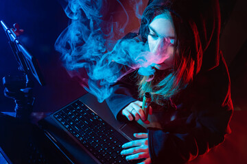 The girl smokes VAPE and uses computer gadgets. A girl on a dark background with an electronic...