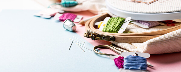 Embroidery set fot cross stitching. White fabric, embroidery hoop, colorful threads, scissors and needls. On blue background. Hobbies concept with copy space, banner. © Iryna Melnyk